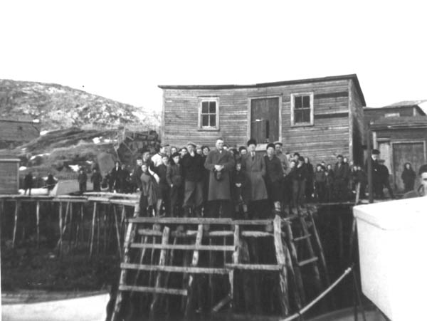 129: Large group of people on McCarthy's wharf. J V McCarthy (center with hat in hands),  Mike Lambe (to left with hand to face), Din-Pat Barry (to right wearing fur hat). (1954)